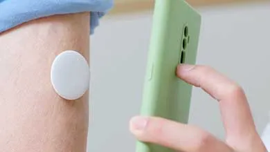 Close-up of a smartphone scanning a white, circular continuous glucose monitor on a person's upper arm.