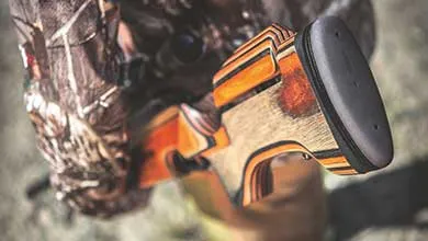 Close-up, overhead view of a rifle buttstock made of laminated wood with orange and black stripes and a black recoil pad.