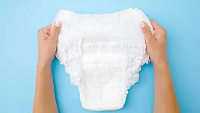 Two hands hold an open white adult diaper against a light blue background.