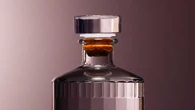 Close-up of a glass bottle’s top, sealed with a cork and a shiny silver cap.