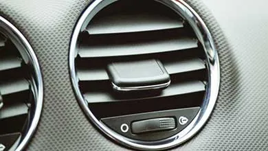 Close-up of a circular car air vent with chrome trim and horizontal slats, set in a textured dashboard.