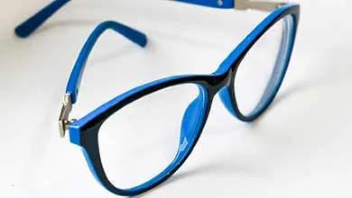 Close-up of black-framed eyeglasses with blue arms resting on a white surface.