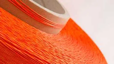 Close-up of a large spool of bright orange thread tightly wound around a cardboard core, showing textured parallel strands against a plain light background.