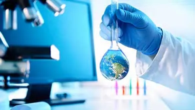 A gloved hand holds a glass flask containing a miniature Earth in a laboratory.