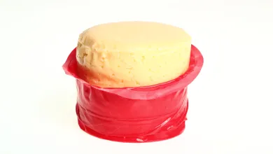 A round, pale yellow cheese partially unwrapped in red wax, exposing the top half.